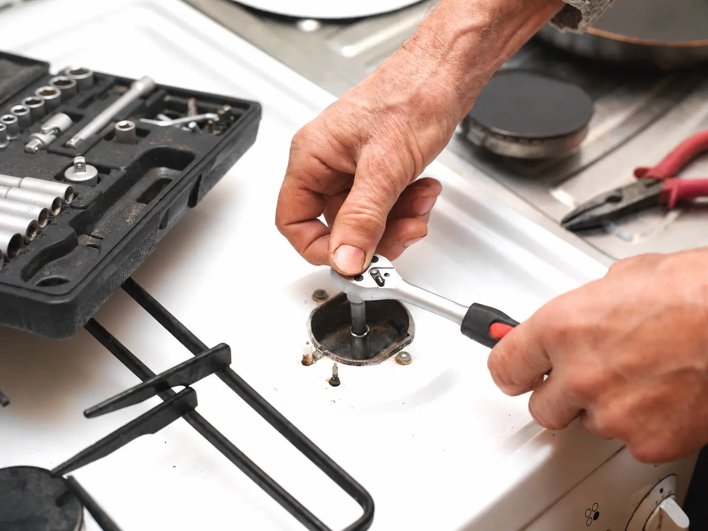 Close-up of a technician repairing a stove igniter on a white gas range using a ratchet wrench
